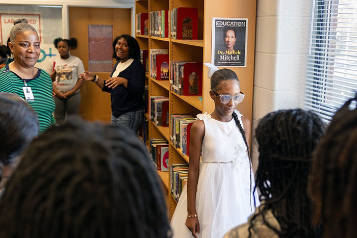 Young girl in white dress presenting to a group of students in a school library