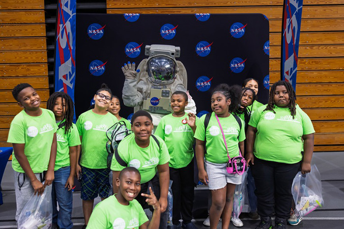 Group of children visiting NASA and posing in front of spacesuit